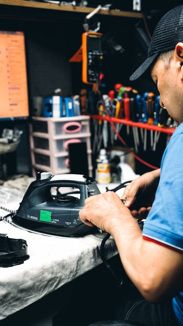 about-01 Technician in workshop repairing an electric iron with tools and equipment in the background.