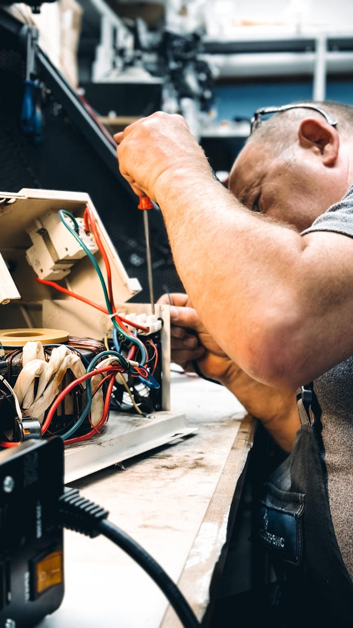 gallery-5 Expert electrician repairing an electrical device in a workshop setting, focusing on wiring.