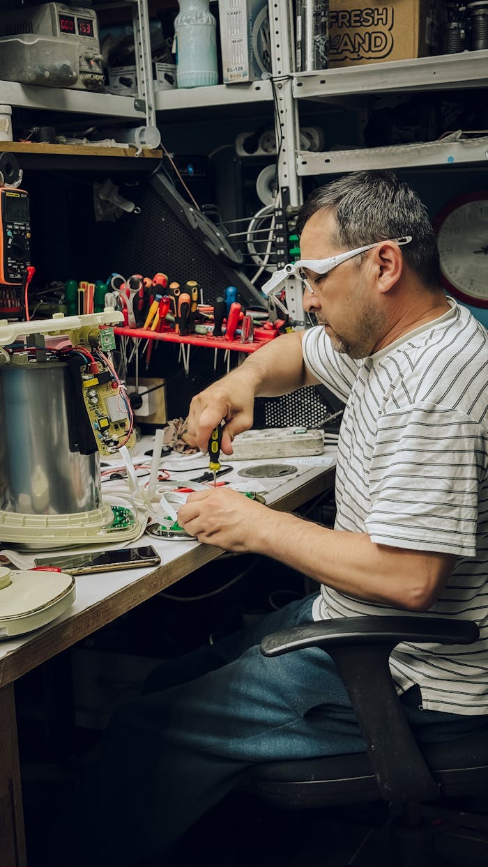 gallery-2 Man working on electronics repair in workshop, surrounded by tools and equipment.